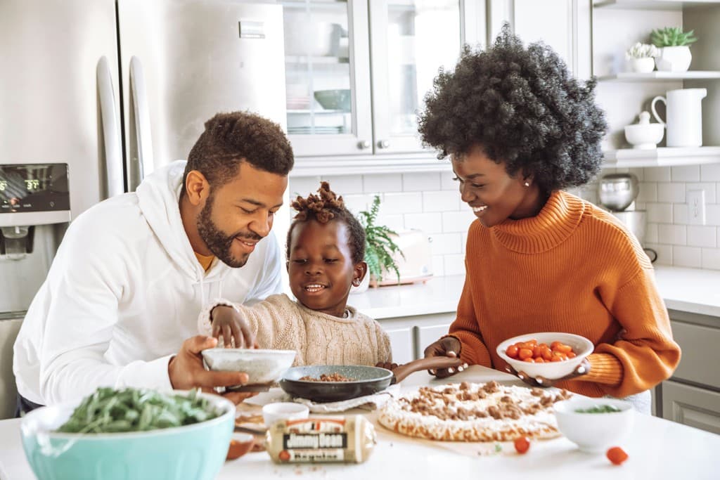 A parent and child preparing food together in a kitchen.